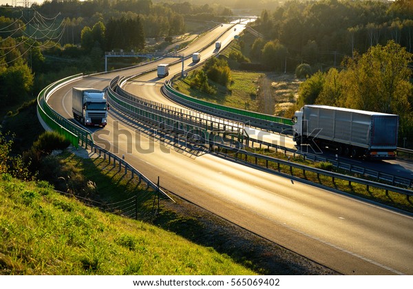 White trucks\
passing through tollgates on the highway winding through the wooded\
valley in backlit. View from\
above.