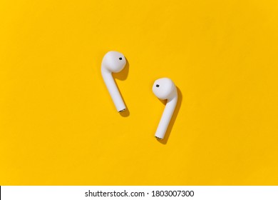 White true wireless headphones or earbud on bright yellow background. Top view