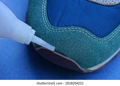 White Tube In Hand Glue The Sock Of A Suede And Leather Sneaker On A Blue Background