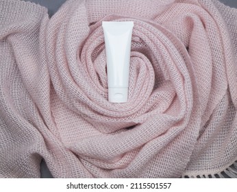 White Tube With Protective, Weather Barrier Cream Or Moisturiser On The Background Of Soft And Warm Pink Shawl With Copy Space. Mockup Plastic Tube