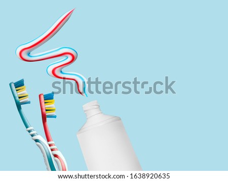 A white tube with three-color toothpaste squeezed out and two toothbrushes on a blue background. A useful habit for children, fighting tooth decay.