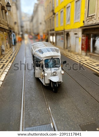 White tuk-tuk vehicle making its way down a narrow, cobblestone street in the historic downtown of Lisbon, Portugal, with tram tracks under its wheels. Selective focus.