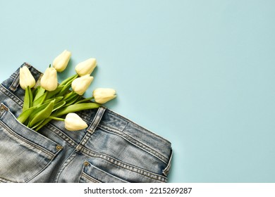 White Tulips In The Pocket Of Jeans On A Light Blue Background. Give A Present To Dad. Happy Fathers Day, Mens Day, Valentines Day Concept. Top View With Copy Space. Flat Lay Composition