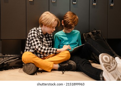 White two boys talking and using tablet computer while sitting on floor at school
