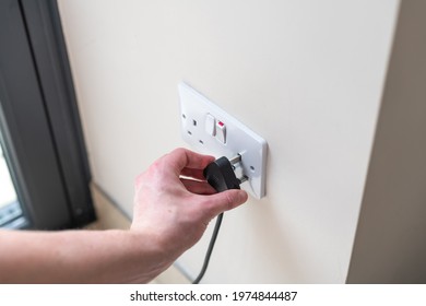 White Uk Plug Sockets Being Plugged Into With A Black Plug And Male Arm