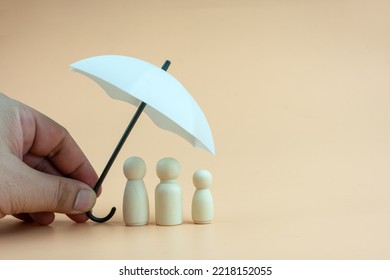 White Umbrella With Wooden Family Peg Dolls For Protection With Copy Space. Family Protection And Insurance Coverage Concept. The Insurance Agent Presents Protection Model That Symbolize The Coverage.