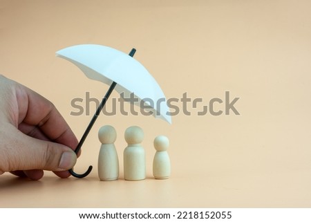 White umbrella with wooden family peg dolls for protection with copy space. Family protection and insurance coverage concept. The insurance agent presents protection model that symbolize the coverage.