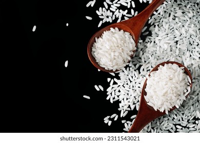 White uncooked rice in wooden spoons on black background. Raw grains of long rice are scattered on table. Natural organic vegan food. Traditional Asian cereal culture. Copy space. - Shutterstock ID 2311543021