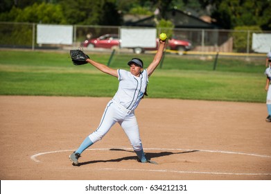 White Uniform Fast Pitch Softball Pitcher Winding Up To Throw In Side View. 