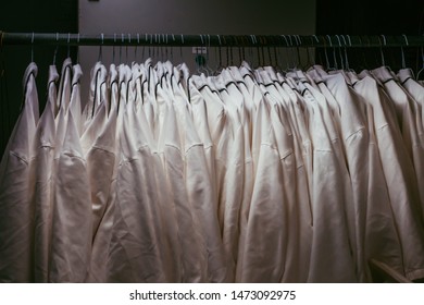 White uniform is hanging in a dark locker. Medical jackets are ready to use. Special textile clothing for a different use. Hospital wardrobe during night time.