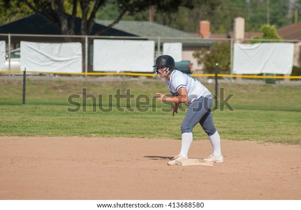 White uniform softball player on second base and\
ready to run.