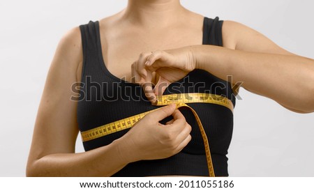 White unrecognizable anonymous lady in black top measures her bust with a tape for bra fitting. Studio no head shot high quality photo image on white background.