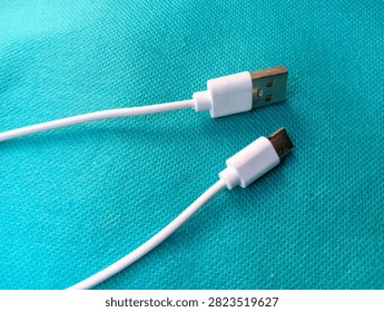 White USB Type-A to USB Type-C charging cable lying on a cyan blue textured background, close-up top view.