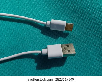 White USB Type-A to USB Type-C charging cable lying on a cyan blue textured background, close-up top view.