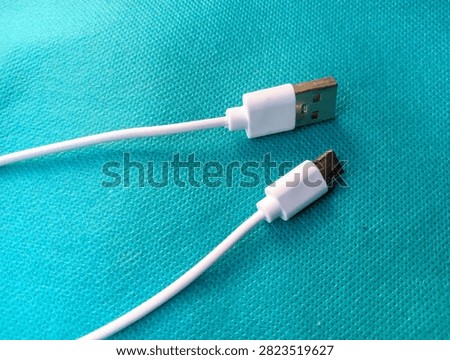 White USB Type-A to USB Type-C charging cable lying on a cyan blue textured background, close-up top view.