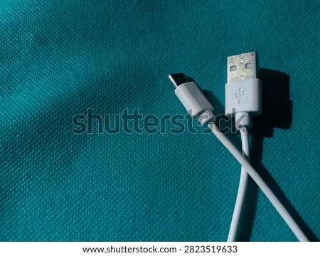 White USB Type-A to USB Type-C charging cable lying on a cyan blue textured background, close-up top view.