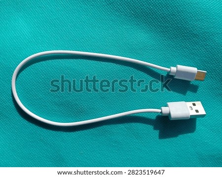 White USB Type-A to USB Type-C charging cable lying on a cyan blue textured background, close-up top view.