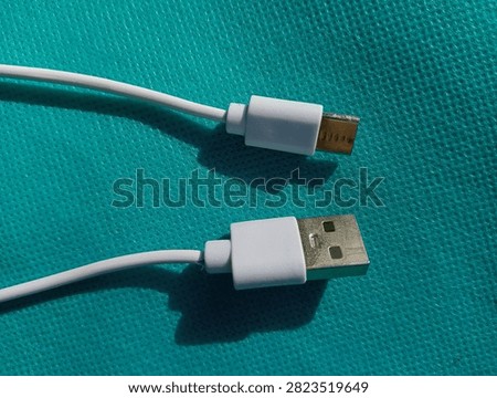 White USB Type-A to USB Type-C charging cable lying on a cyan blue textured background, close-up top view.