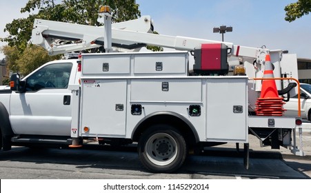 White Utility Truck With Cherry Picker Parked In Parking Lot. Blue Sky And Tree Background. Horizontal.