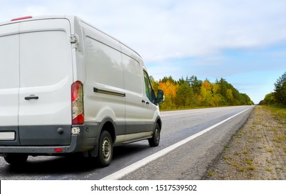 White Van Moving On Asphalt Road In The Countryside On Autumn Landscape Background. Small Truck Delivers The Goods