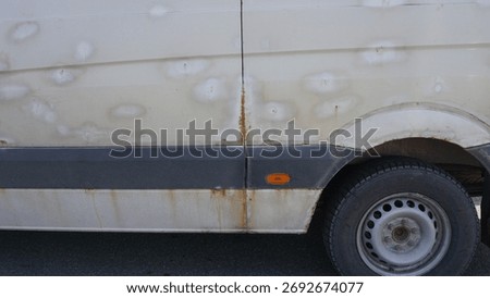 White van in poor condition shows rust, dents. The aged vehicle sits in a sunlit parking lot, conveying neglect, fatigue, and industrial grit. Car in need of repairs
