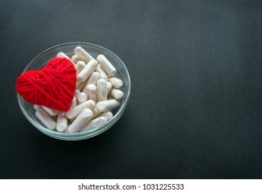 White Veg Capsules And Red Thread Heart In Glass Bowl On Black Background. Anticoagulant, Blood Thinners. Cardiac Medications, Pills For The Heart. Treat Heart Disease Failure