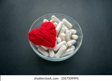 White Veg Capsules And Red Thread Heart In Glass Bowl On Black Background. Anticoagulant, Blood Thinners. Cardiac Medications, Pills For The Heart. Treat Heart Disease Failure