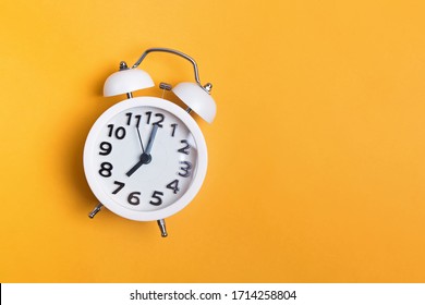 White vintage alarm clock on yellow color background, top view with copy space