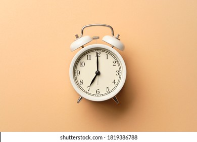 White vintage alarm clock on pastel orange paper background that show time at 7:00 o'clock.