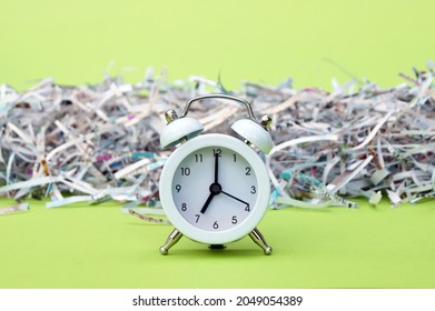 A white vintage clock in the foreground of 7:00 am on a light green background. Shredded paper in the background.