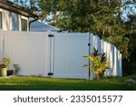 White vinyl picket fence on green lawn surrounding property grounds for backyard protection and privacy
