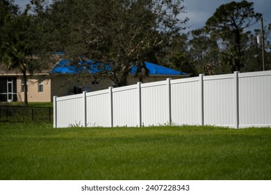 White vinyl picket fence on green lawn surrounding property grounds for backyard protection and privacy