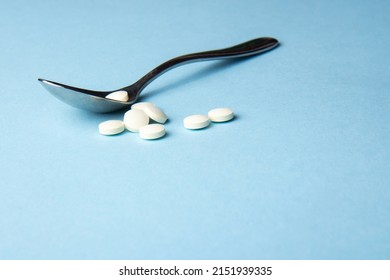 White vitamin tablets on iron lack spoon on a blue background. Dietary supplements. Complementary and medical products