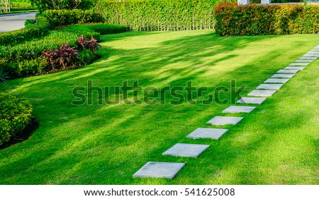 White walkway sheet in the garden, green grass with cement path  Contrasting with the bright green lawns and shrubs, shadows, trees, and morning sun Garden landscape design, lawn care service.