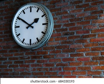 White wall clock on a red brick wall is the background.