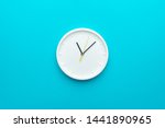 White wall clock with yellow second hand hanging on the wall. Minimalist flat lay image of plastic wall clock over blue turquiose background with copy space and central composition.