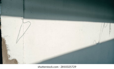 A white wall featuring the contrast between sunlight and sharp shadows. Faint shadows of objects—such as a cable or a hanger—are also visible on the right side.