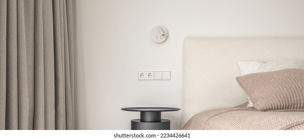 White wall lamp above the bed, metal beside table, white electrical outlet, oak wooden floor.
Modern minimalist aesthetic bedroom interior design in warm shades