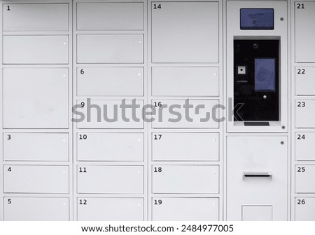 A white wall with numbered boxes and a machine in the middle. The machine has a screen and a keypad