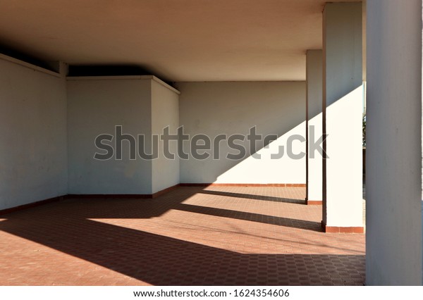 White wall, terracotta tiled floor and\
columns in the entrance of a residential building. Oblique shadow\
divides the scene. Background for copy\
space