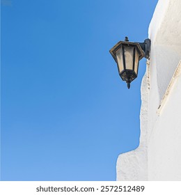 white wall under a cloudless deep blue sky and a cast iron lantern on the wall facade in the village of Mijas in Spain.