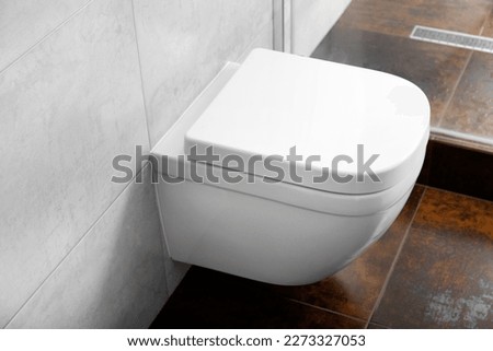 White wall-mounted toilet bowl in a modern bathroom interior, hanging toilet bowl on a gray wall.