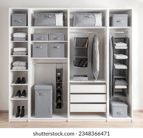 White wardrobe with various clothes and gray storage bins for accessories. The wardrobe features white wooden shelves - Powered by Shutterstock