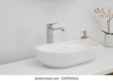 White washbasin, orchid flowers and soap dispenser in bathroom. Interior design