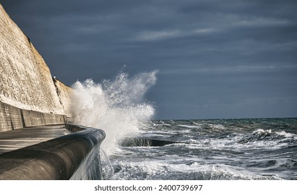 White waves breaking against the sea defences below the white chalk cliffs under leaden grey skies on a stormy windy rough sea
