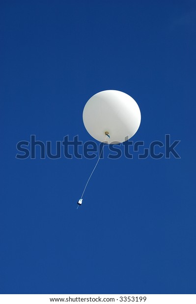 A\
white weather balloon is ascending into the blue sky. Picture was\
taken during a 3-month Antarctic research\
expedition.