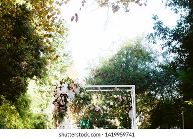 White Wedding Arbor At Garden Ceremony With Roses Orchids And Greenery