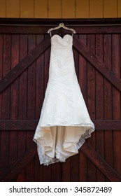 White Wedding Dress Hanging On Large Maroon Stained Doors At A Winery In Oregon.