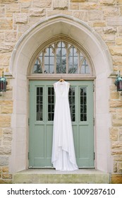 White Wedding Dress Hangs On A Green Church Door