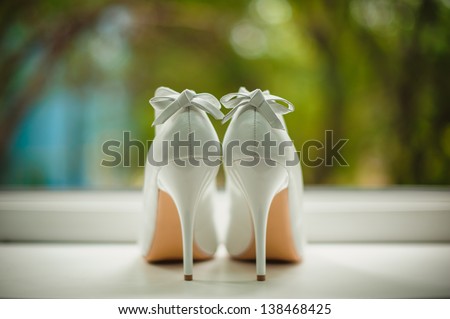 white wedding shoes with a bow on a heel on a green background